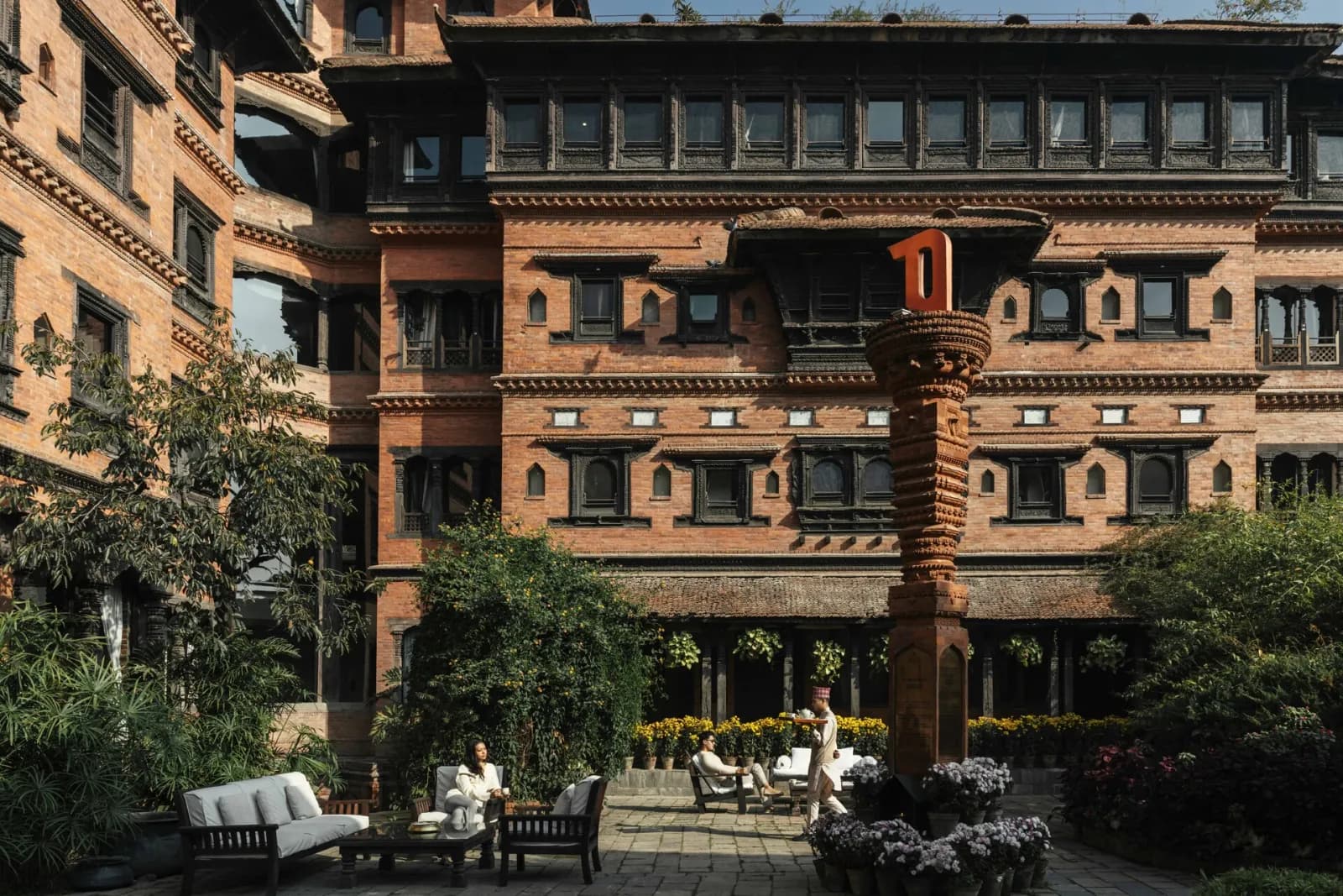 Guests relaxing in the brick courtyard of The Dwarika’s Hotel, Kathmandu, beneath carved Newari windows