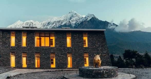 The stone front of Shinta Mani Mustang lit up at dusk, with a golden yak sculpture and snow peaks behind
